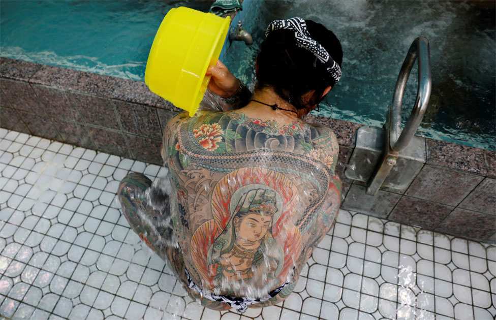 Мужчина с татуировками на теле льет воду себе на спину