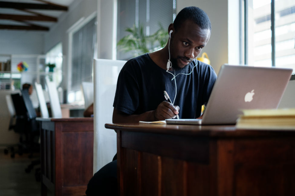 Молодой черный южноафриканец сидит за компьютером