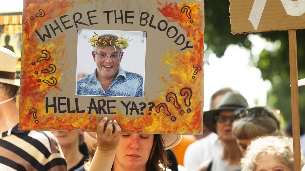 Протестующий в Сиднее держит вывеску возле дома премьер-министра с фотографией Скотта Моррисона и надписью: «Где, черт возьми, я?»