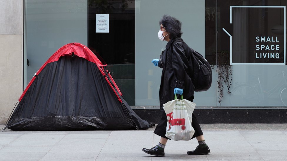 Женщина проходит мимо палатки бездомного, установленной возле мебельного магазина