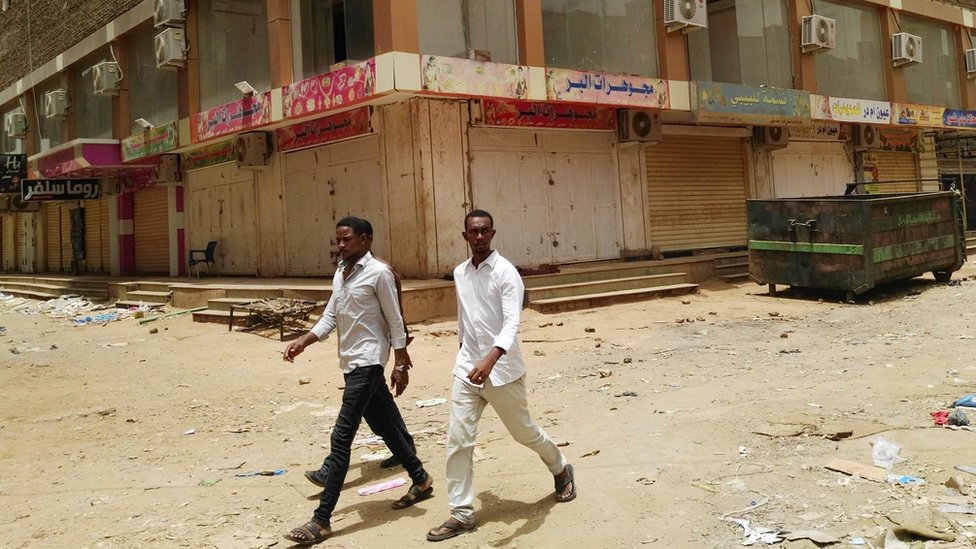 مجموعة من الرجال يسيرون في سوق المدينة بأم درمان بالخرطوم والمحلات مغلقة