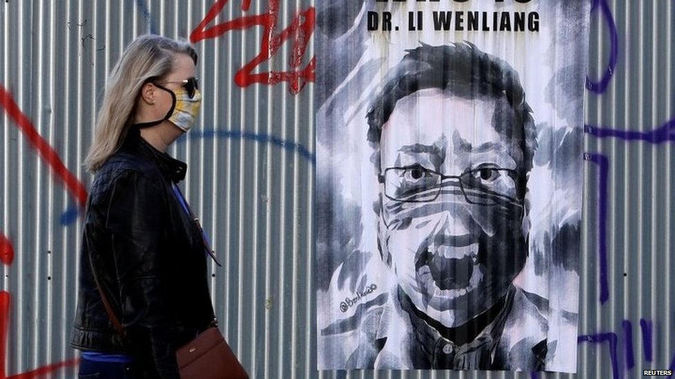 A woman wearing a face mask walks past a poster of late Li Wenliang in Prague