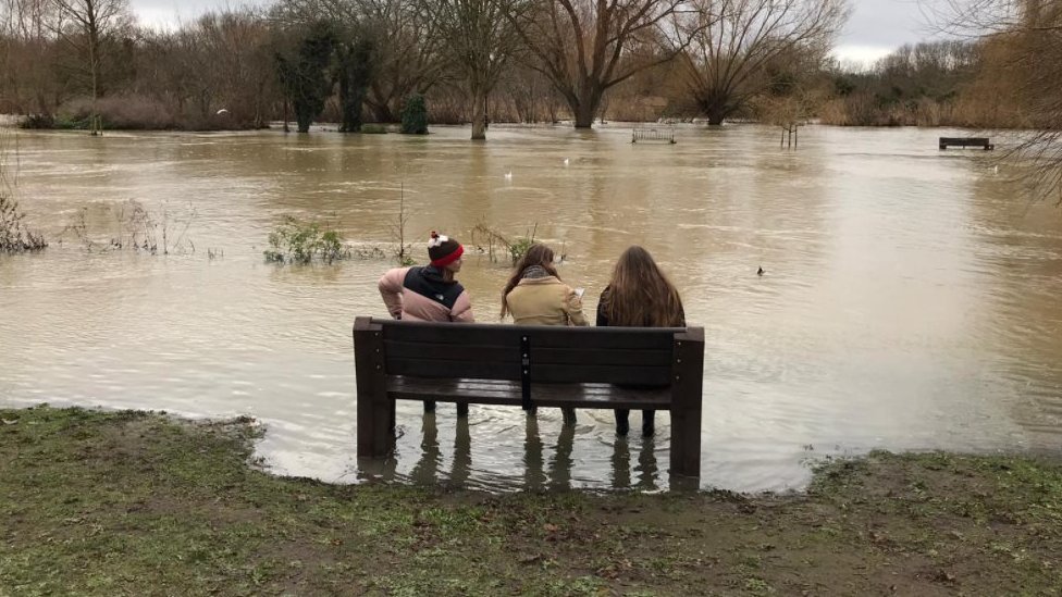 Three women sat on bench in floodwaters in Bedford