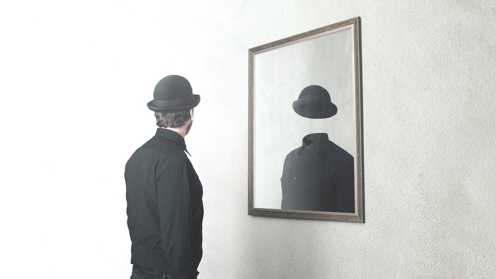 Hombre frente a un espejo en el que no se ve su rostro.