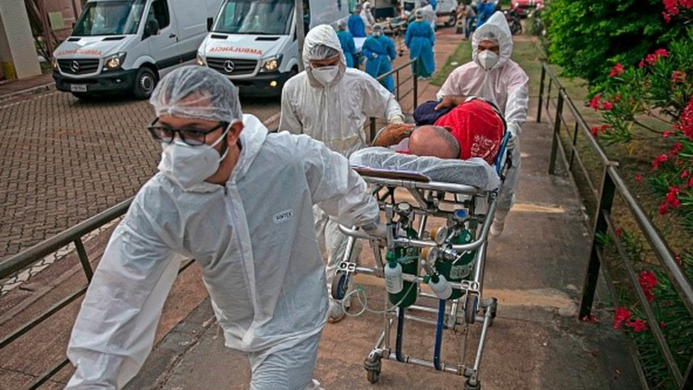 Profissionais da saúde carregam paciente em maca para dentro de um hospital