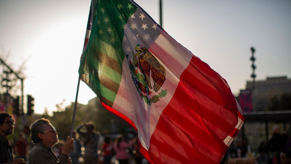 Un hombre sostiene las banderas de México y Estados Unidos.