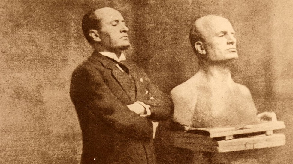 Mussolini posa junto a un busto.