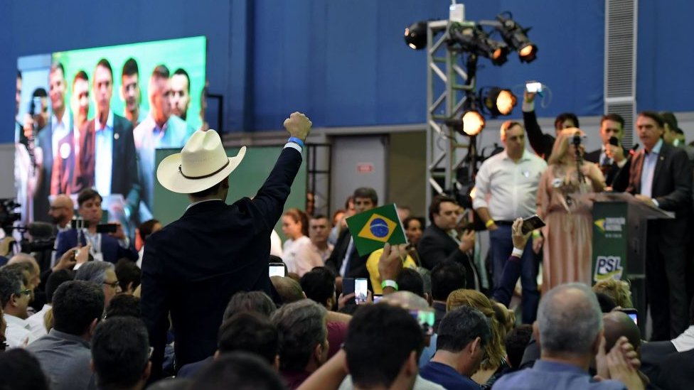 Homem com chapéu de fazendeiro acena em evento com Jair Bolsonaro