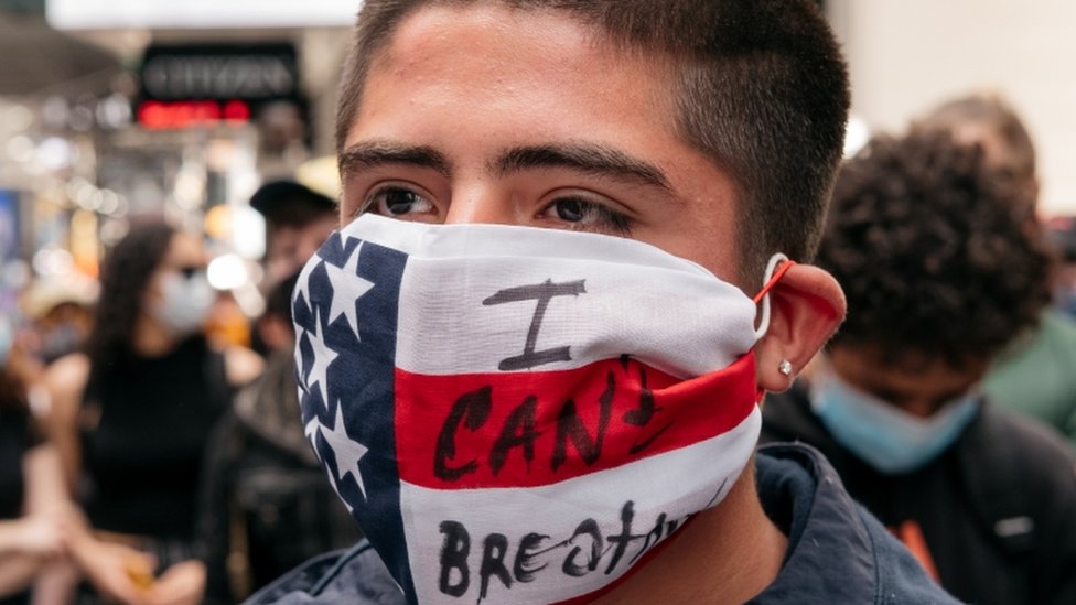 Un manifestante con una mascarillas con la bandera de Estados Unidos y la leyenda:"No puedo respirar".