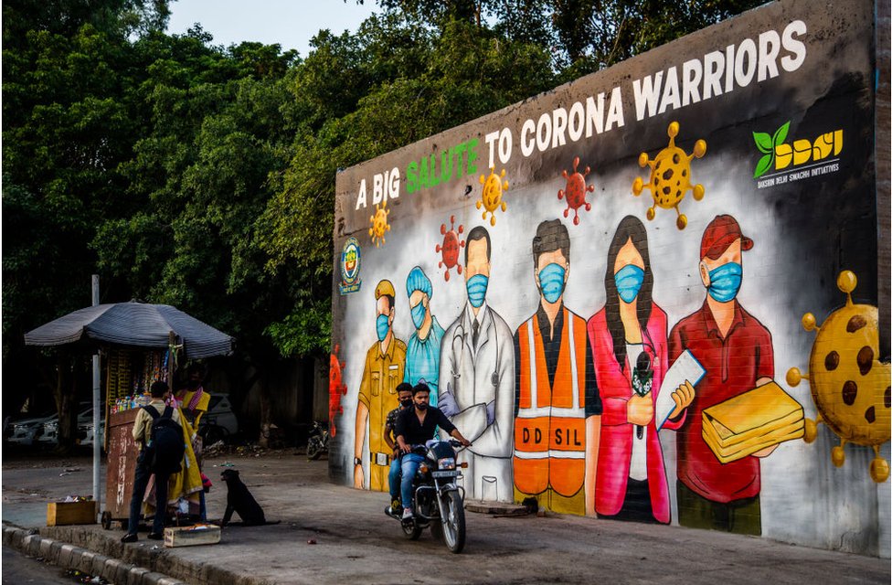 Мотоциклист проезжает мимо фрески, посвященной индийским «воинам ковидов» в Дели 8 июня