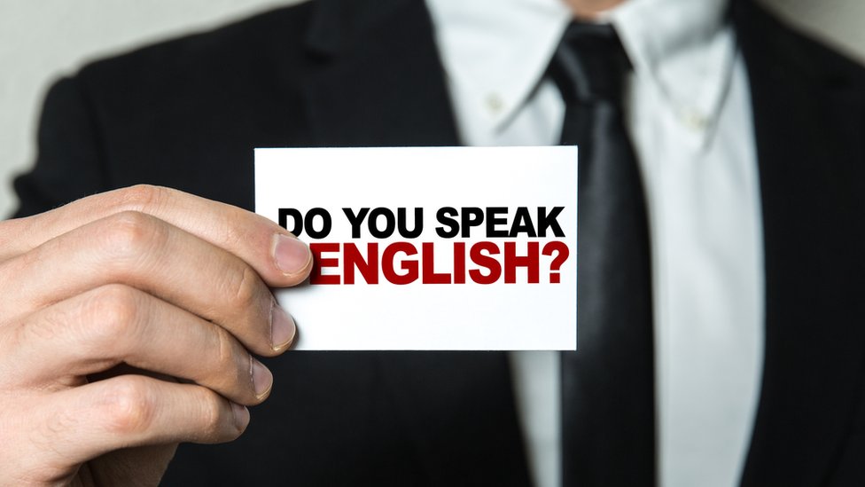 Un hombre sostiene un cartel que dice Do you speak English?