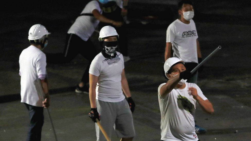 Люди в масках в белых футболках, вооруженные палками, после нападения на протестующих против закона об экстрадиции после демонстрации. Юэнь Лонг, Гонконг