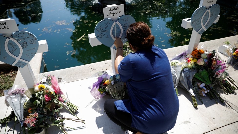 Una mujer en cuclillas frente a los adornos de homenaje a las víctimas del tiroteo en Uvalde