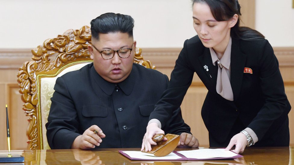 На изображении показан северокорейский лидер Ким Чен Ын, которому помогает его сестра Ким Ё Чжон