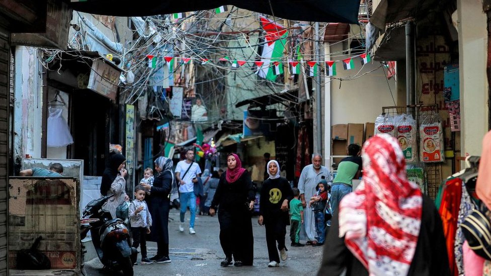 Palestinian flags hang above pedestrians walking along an alley at the Shatila camp for Palestinian refugees in the southern suburb of Beirut