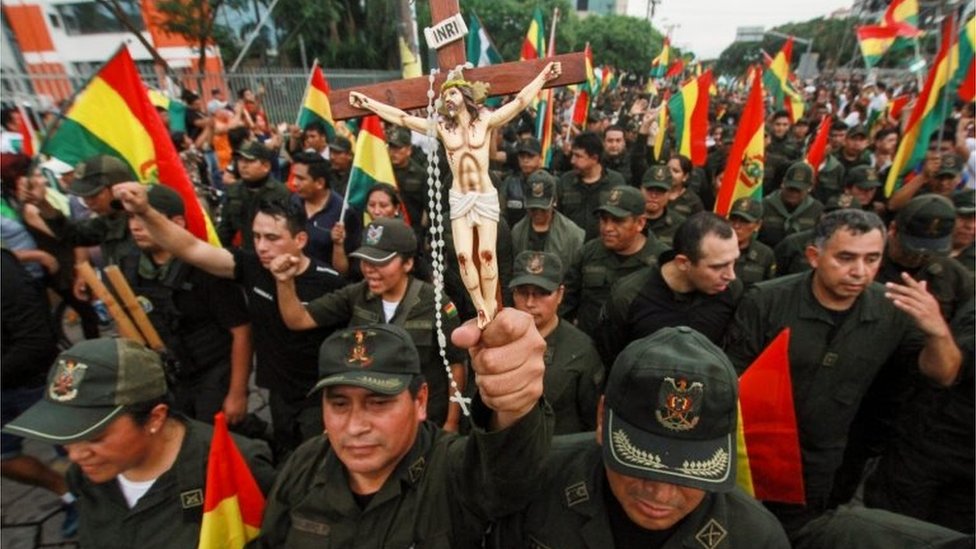 Офицер полиции держит распятие среди товарищей и людей, вышедших на улицы Санта-Крус, чтобы отпраздновать отставку президента Боливии Эво Моралеса 10 ноября 2019 года.
