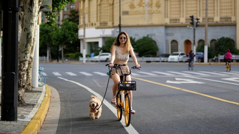 Image shows woman cycling with a dog