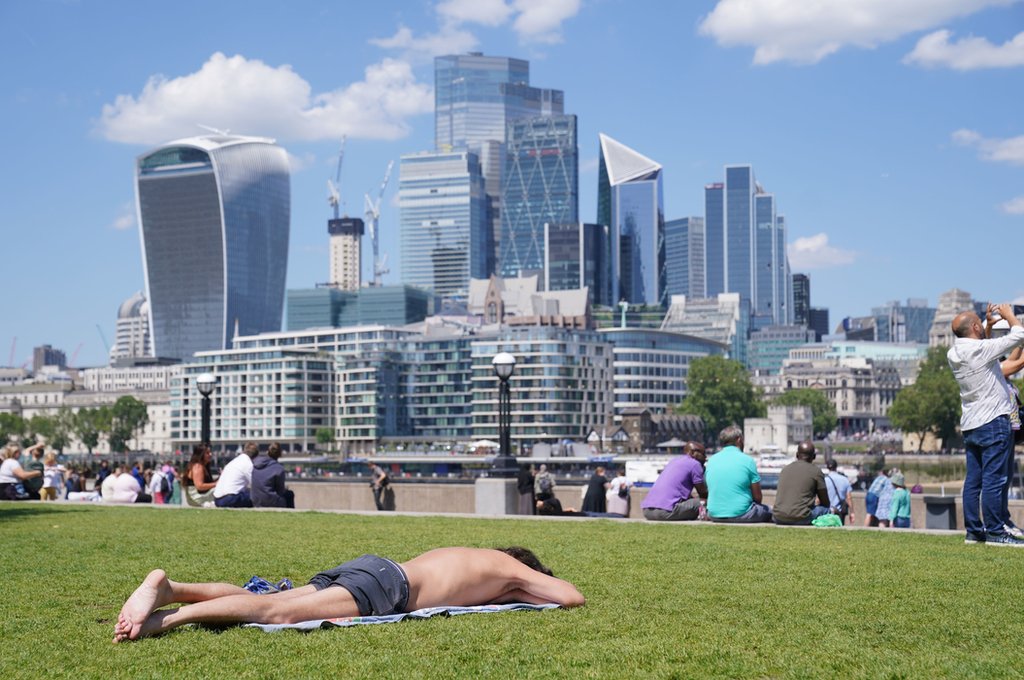 A man lies in the sun as people enjoy the hot weather with a view of the city of London skyline from Potters Fields Park in London - August 11, 2023.