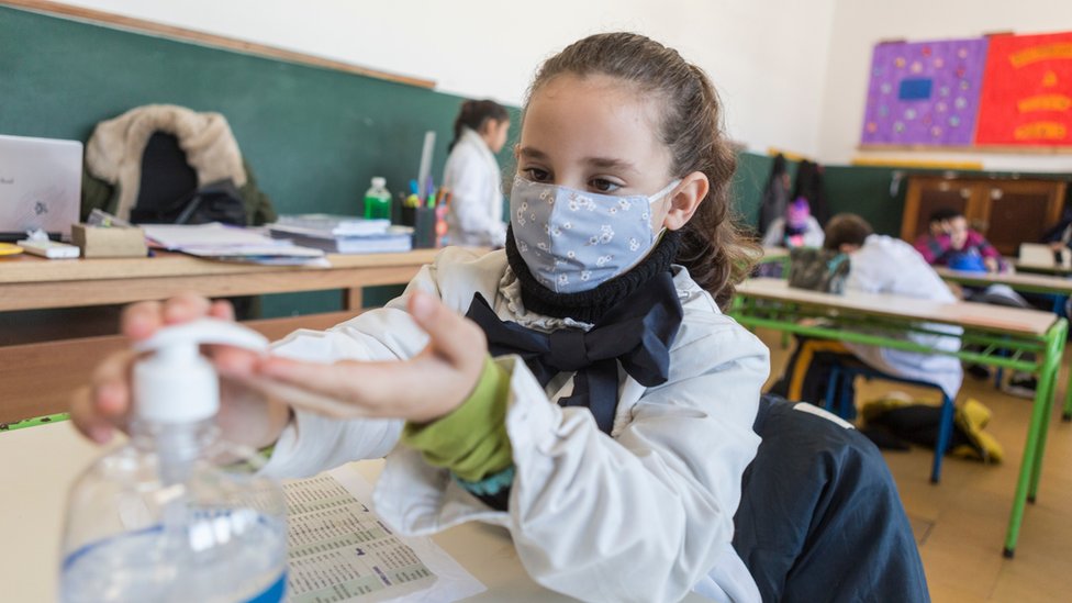 Una niña en una escuela en Uruguay con mascarillas poniéndose gel con alcohol en las manos