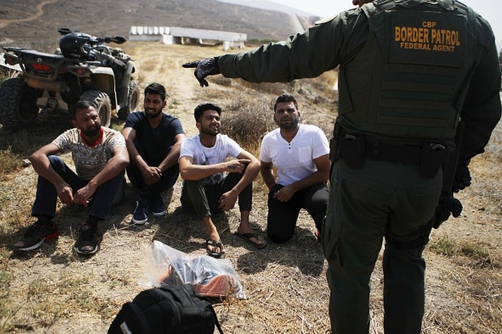 Агент пограничного патруля США наблюдает за группой задержанных мужчин из Индии, которые незаконно пересекли границу США и Мексики 16 июля 2018 года в Сан-Диего, Калифорния. По всей юго-западной границе было 34 114 США.Количество задержанных сотрудников пограничной службы в июне по сравнению с 40 338 в мае.