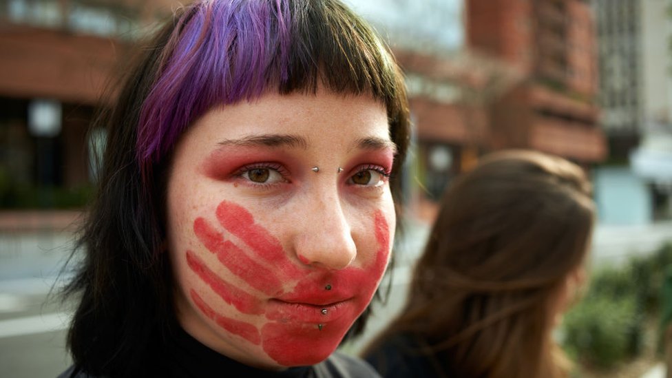 Chica joven con una mano roja pintada en la cara
