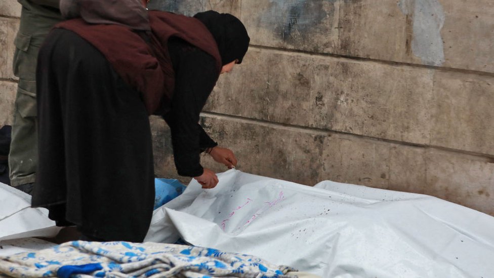 Una mujer siria revisa un cuerpo tendido en la calle frente a un depósito de cadáveres en la ciudad de Alepo tras un terremoto mortal el 6 de febrero de 2023.