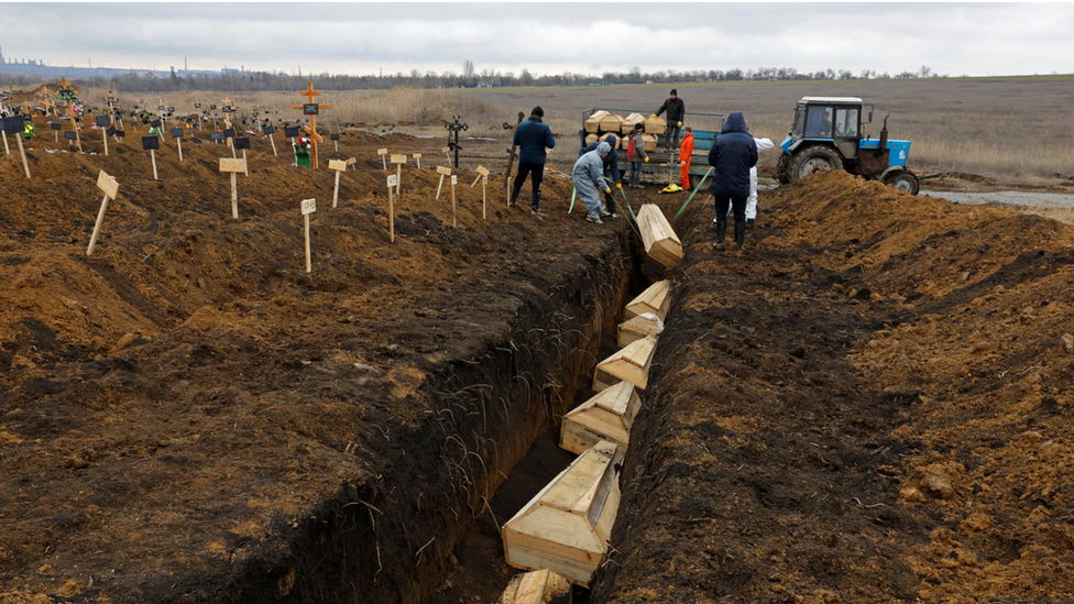 Coffins are placed into a long trench outside Mariupol in February 2023