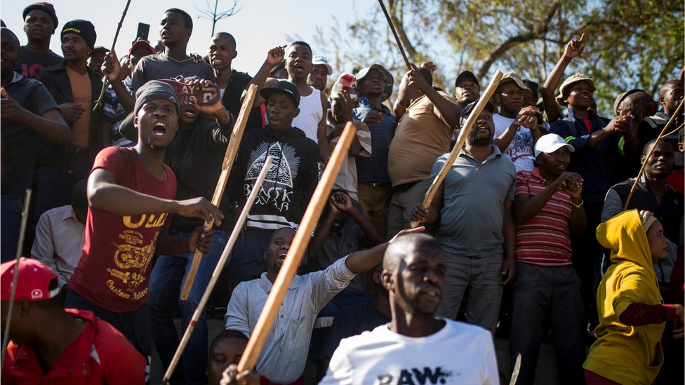 Группа зулусских мужчин, проживающих в хостеле Jeppe, кричит и машет палками во время выступления министра полиции генерала Беки Селе в Джеппстауне 3 сентября 2019 года в Йоханнесбурге.