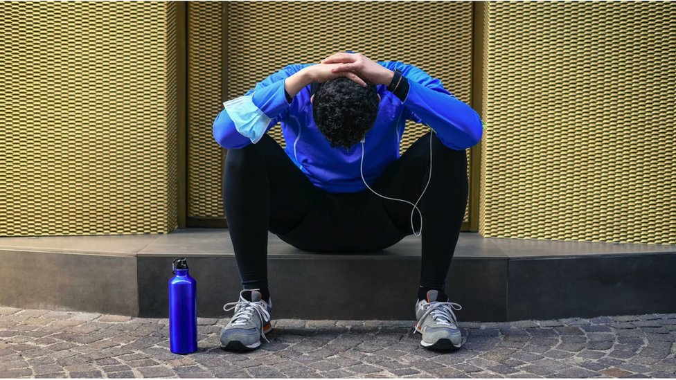 A jogger holds his head in his hands as he sits on a step and looks to the floor