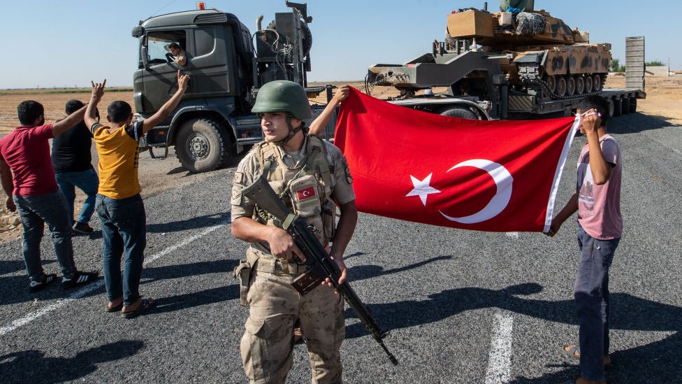 People hold a Turkish flag as they give their support to the Turkish military during the deployment of tanks to Syria