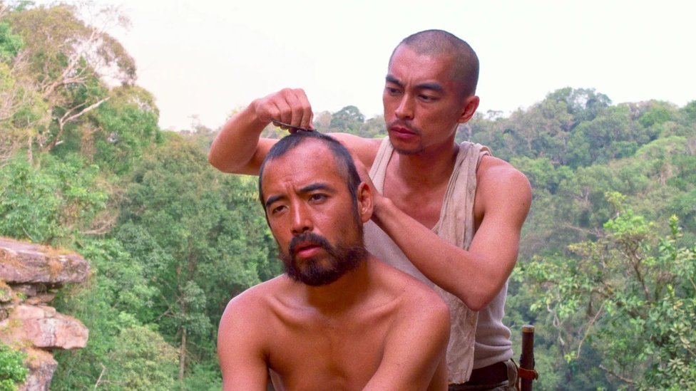 Homem corta o cabelo de outro no meio da selva
