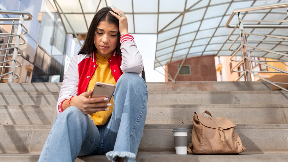Una adolescente mirando su celular con expresión de angustia en el rostro.