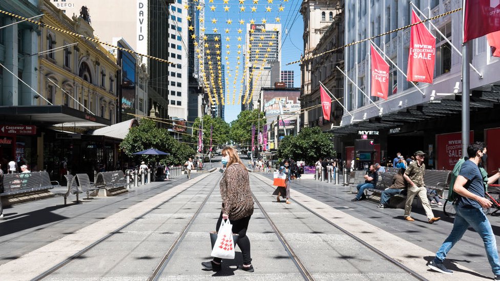 Покупатели в масках пересекают торговый центр Bourke Street в центре Мельбурна в День подарков 2020 года