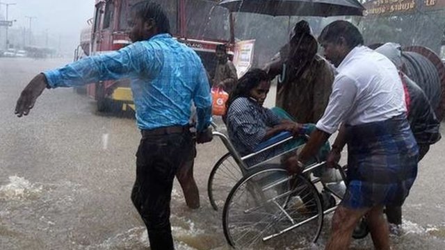 People assist person in a wheelchair through waterlogged streets in Chennai