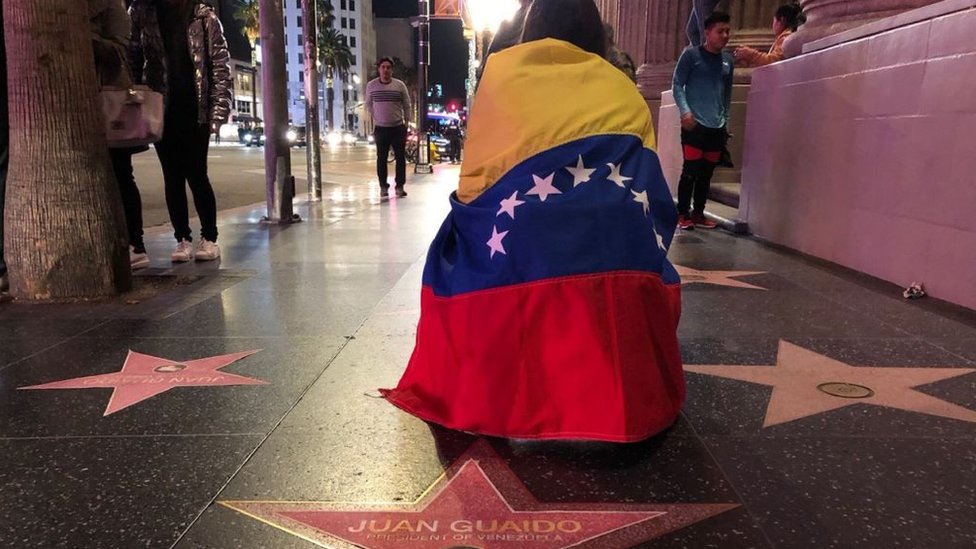Una mujer está de rodillas y arropada con una bandera de Venezuela en el Paseo de la Fama de Hollywood.
