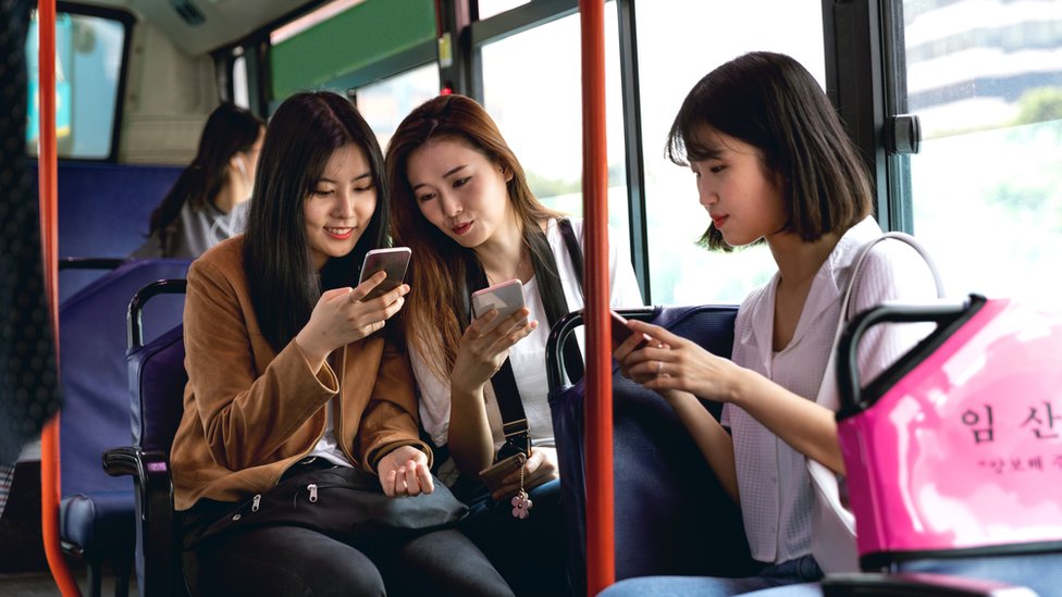 Tres chicas mirando sus celulares en un tren de Corea del Sur.