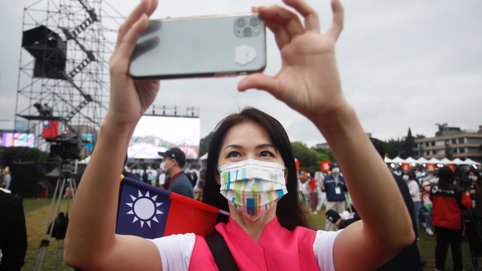 A participant with a Taiwanese flag takes pictures using an iPhone during Taiwan"s National Day celebrations outside the Presidential Palace in Taipei, Taiwan, 10 October 2022
