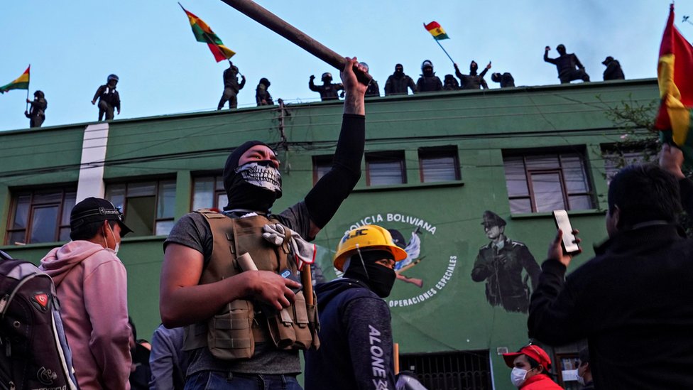 Противники президента Боливии Эво Моралеса реагируют, когда полицейские стоят на крыше своей штаб-квартиры в Кочабамбе, Боливия