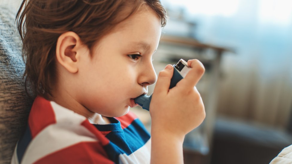 Un niño tomando un inhalador para el asma.