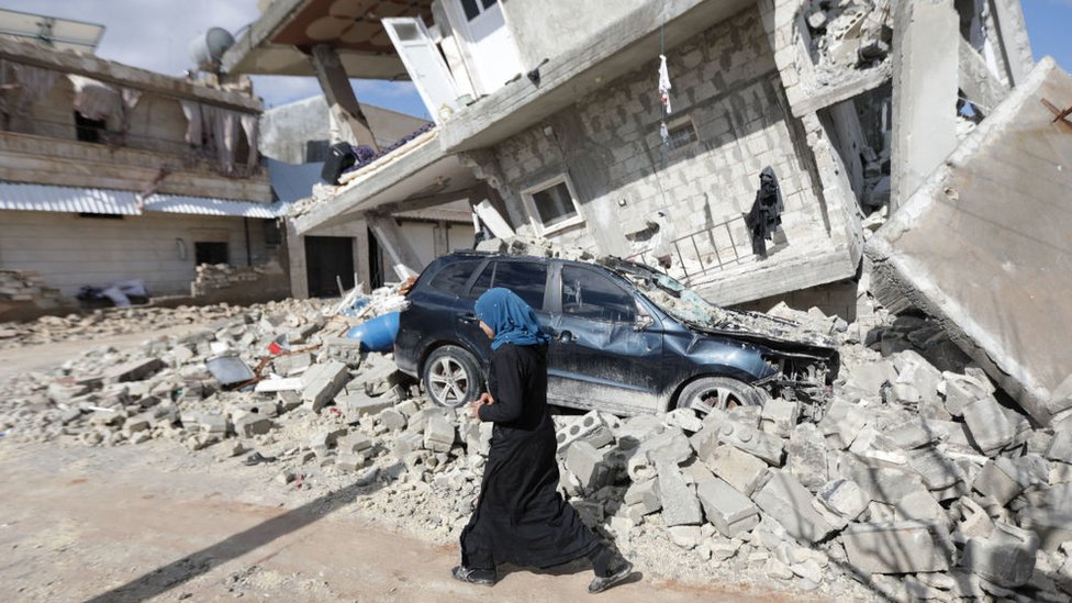 Una mujer siria pasa frente a una casa derrumbada en la ciudad de Azaz, en la frontera de Siria con Turquía, el 7 de febrero de 2023.