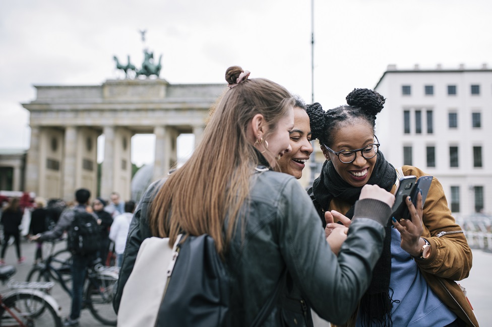 Young people look at a phone next to Berlin's Brandenburg Gate