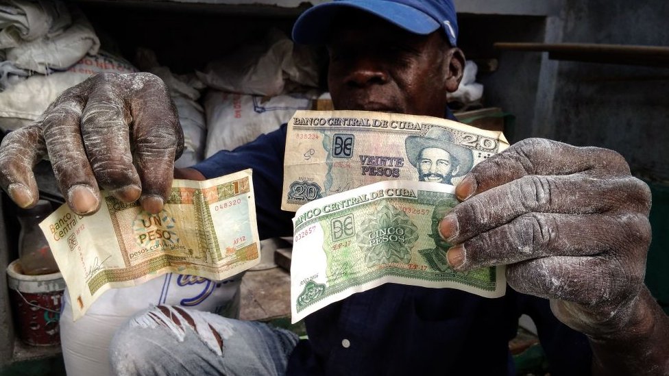 Un hombre muestra billetes de pesos convertibles y pesos cubanos.