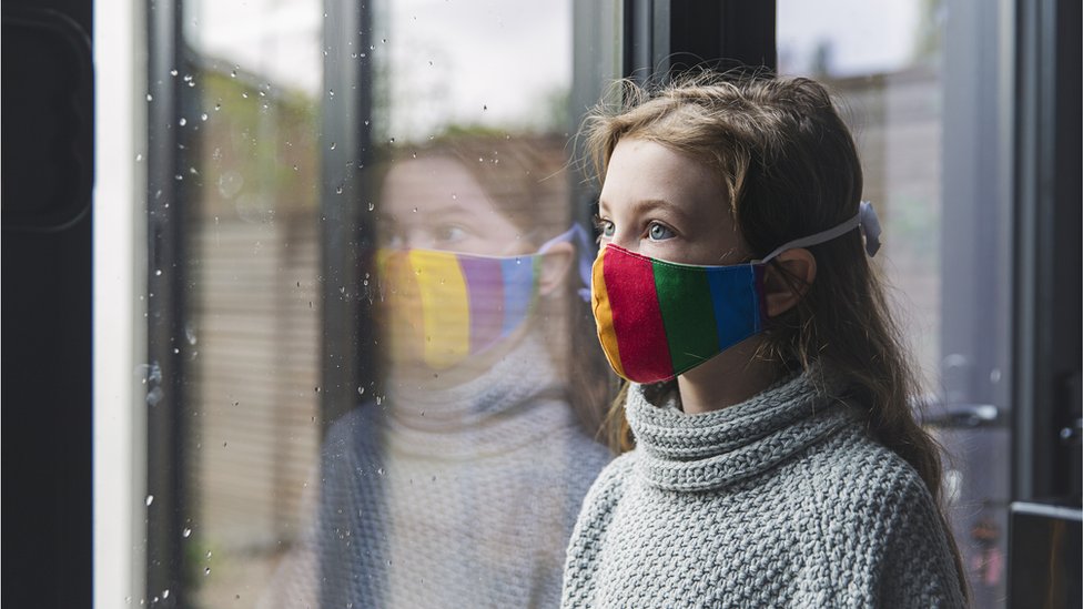 Girl wearing mask stands at a window