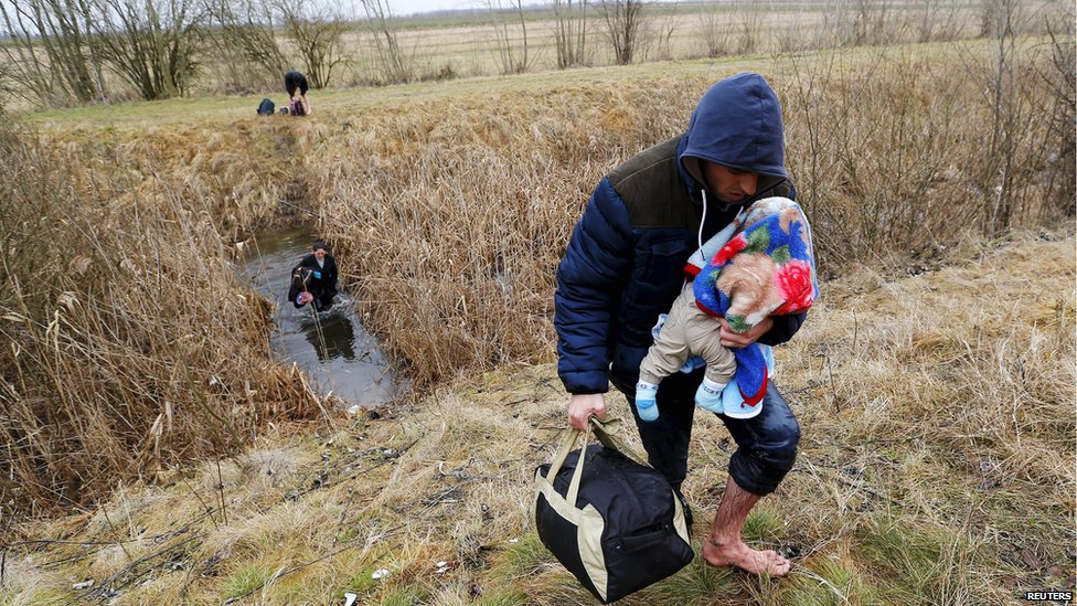 Мужчина из Косово пробирается через воду, неся своего ребенка, когда они незаконно пересекают венгерско-сербскую границу недалеко от деревни Асоттхалом, Венгрия, 6 февраля 2015 г. фото из архива