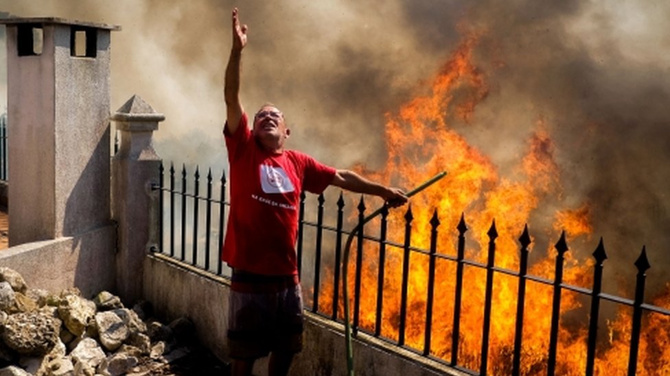 Man pours water on to the flames during a forest fire in Canecas, outskirts of Lisbon, Portugal, 10 July 2022