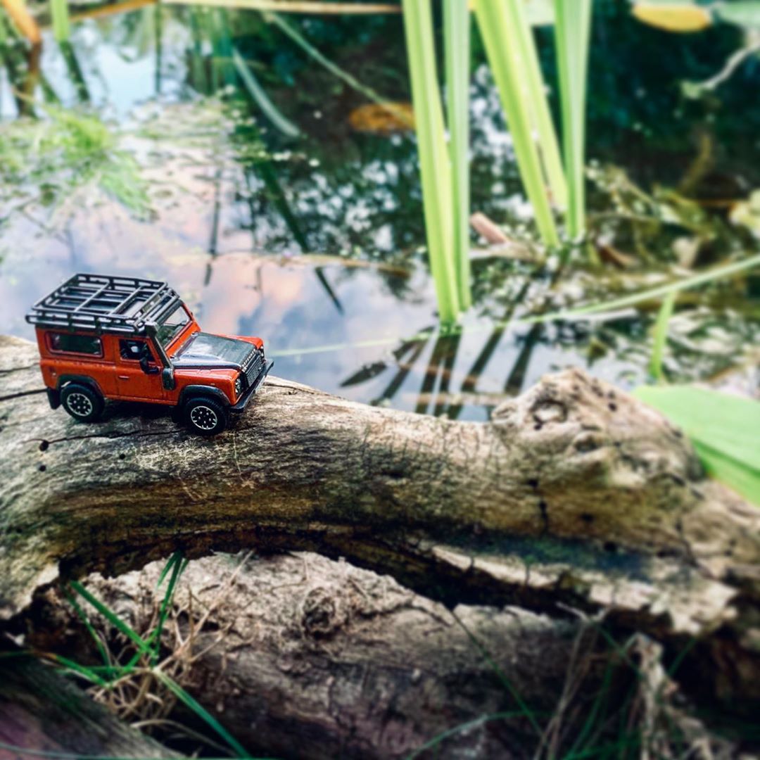 Красная модель Land Rover пересекает воду по ветке