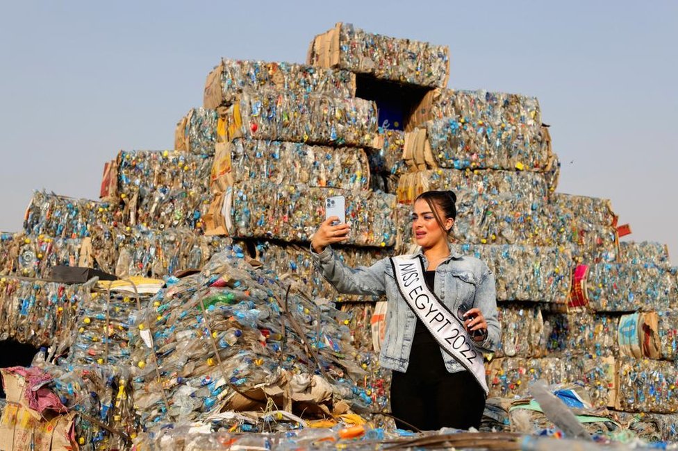 ملكة جمال مصر، هاجر محمد، ترتدي سترة جينز وفستان أسود وتلتقط صورة أمام جبل من النفايات البلاستيكية وهي ترتدي وشاح كتب عليه: ملكة جمال مصر 2022.