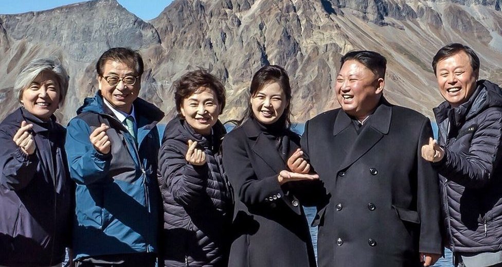 Los presidentes de Corea del Norte y Sur junto a otras personas forman un símbolo del corazón con los dedos.
