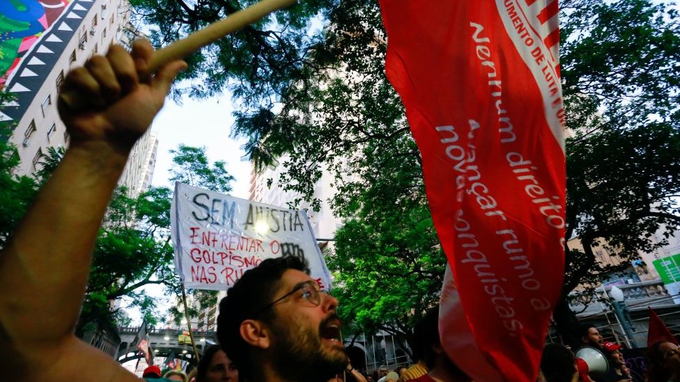 بايدن يمضي على خطى رؤساء أمريكيين عظماء - فايننشال تايمز 2 أعضاء من الحركات الاجتماعية يحتجون دفاعاً عن الديمقراطية في بورتو أليغري، جنوب البرازيل، في 9 يناير/ كانون الثاني 2023، بعد يوم من غزو أنصار الرئيس البرازيلي اليميني المتطرف جاير بولسونارو الكونغرس والقصر الرئاسي والمحكمة العليا في برازيليا.