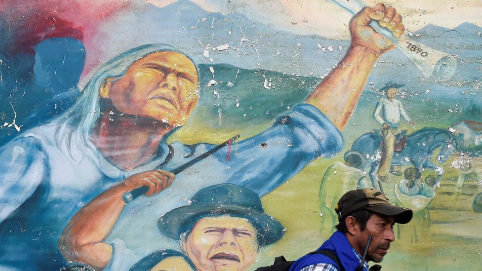 Коренной житель идет рядом с фреской 30 октября 2019 года, во время встречи после недавнего убийства лидера коренных народов и четырех охранников подозреваемыми повстанцами, недалеко от контрольно-пропускного пункта в Такуэйо, в сельской местности Торибио, департамент Каука. Колумбия.